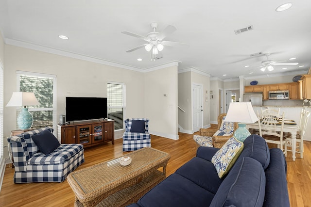 living area featuring light wood-style flooring, a ceiling fan, visible vents, and baseboards