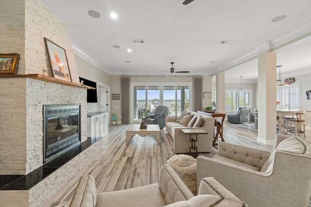 living area with light wood-type flooring, a large fireplace, visible vents, and ornamental molding