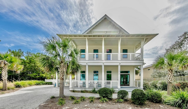 view of front facade with a balcony, covered porch, driveway, and fence