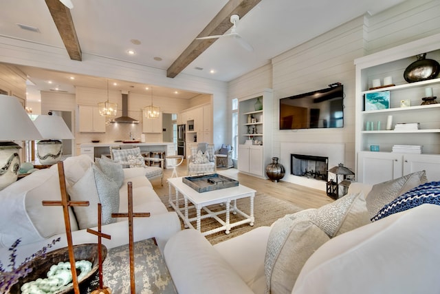 living area featuring light wood finished floors, visible vents, a large fireplace, and beamed ceiling