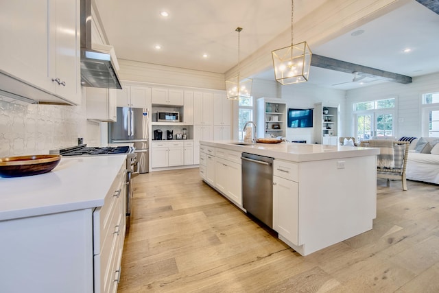 kitchen featuring light wood finished floors, appliances with stainless steel finishes, open floor plan, a sink, and wall chimney exhaust hood