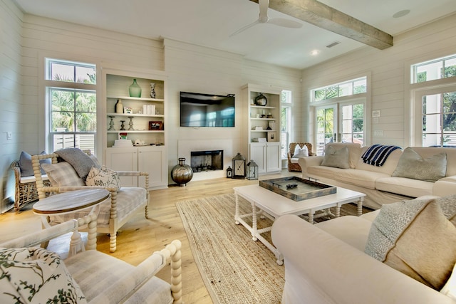 living area featuring visible vents, beamed ceiling, wood walls, light wood-style floors, and a fireplace