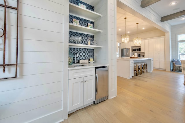 bar featuring light wood-style flooring, a sink, appliances with stainless steel finishes, beam ceiling, and decorative light fixtures