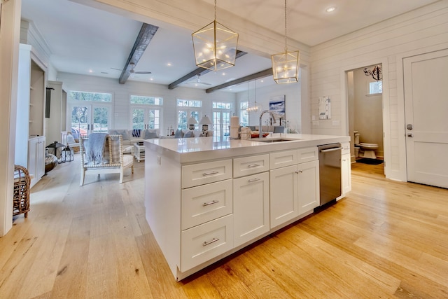 kitchen with white cabinets, light wood-style flooring, open floor plan, hanging light fixtures, and a sink