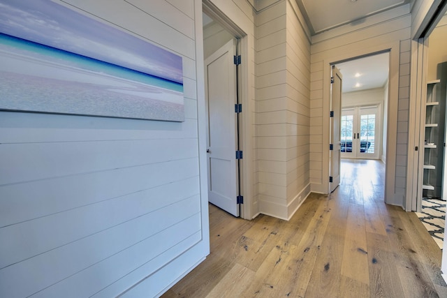 corridor with wooden walls, hardwood / wood-style floors, and french doors