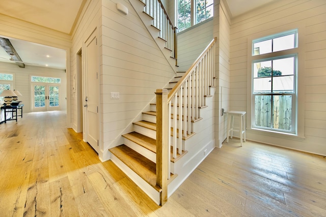 stairs with french doors, wood walls, and wood-type flooring