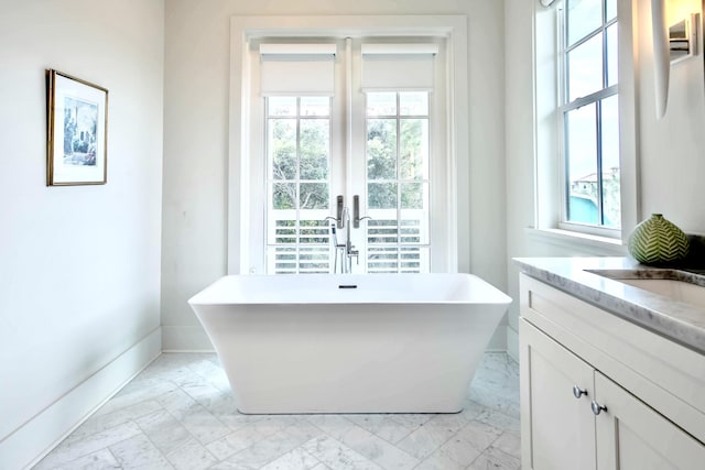 bathroom with marble finish floor, a soaking tub, vanity, and baseboards