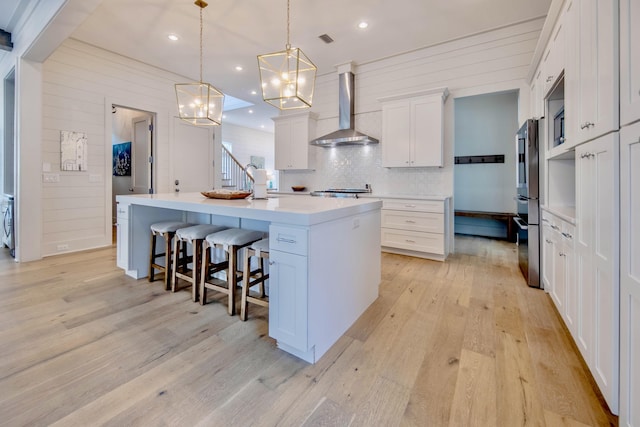 kitchen with a center island, light wood finished floors, light countertops, white cabinetry, and wall chimney exhaust hood