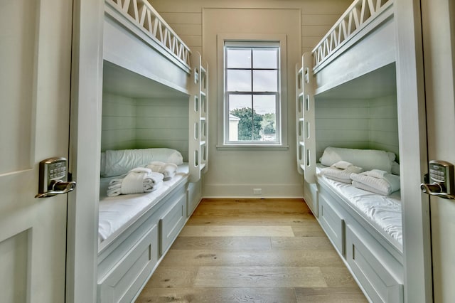 bedroom featuring wood walls, light wood-style flooring, and baseboards