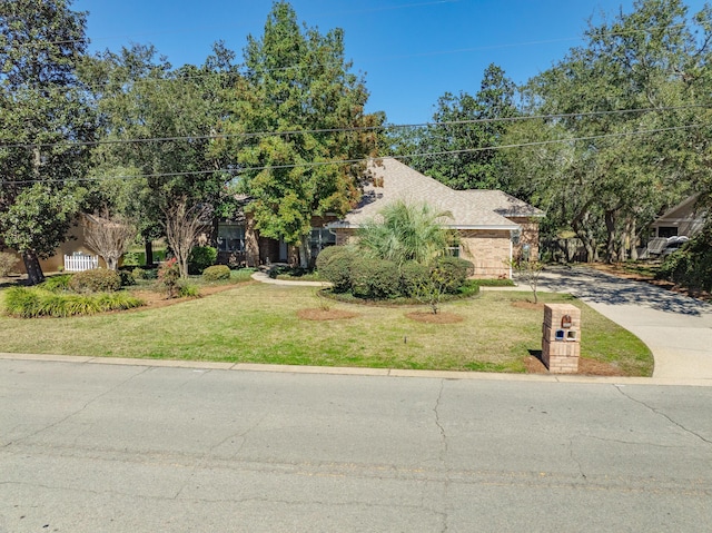 view of property hidden behind natural elements featuring concrete driveway and a front lawn