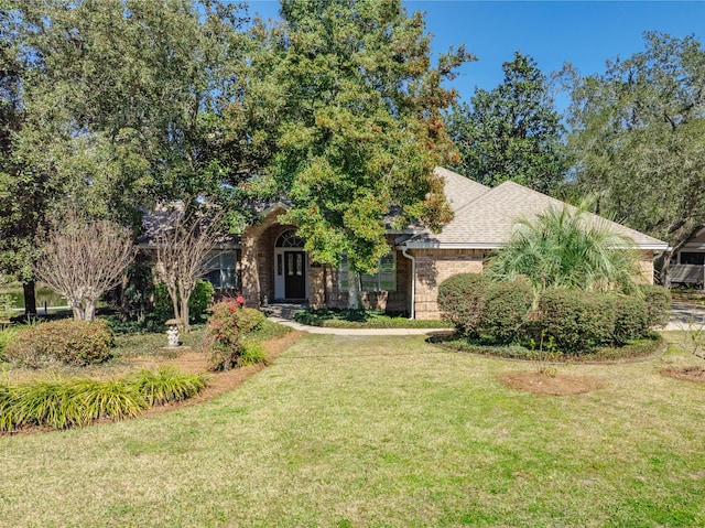 obstructed view of property with a front lawn, a shingled roof, and brick siding