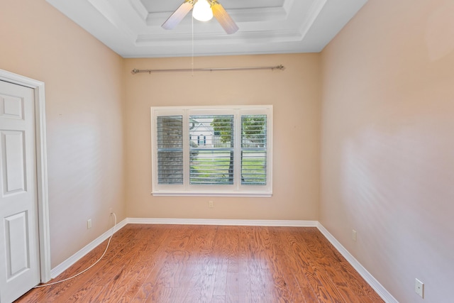 spare room with a ceiling fan, wood finished floors, baseboards, crown molding, and a raised ceiling