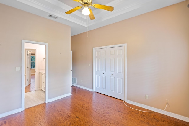 unfurnished bedroom featuring a tray ceiling, baseboards, visible vents, and light wood finished floors