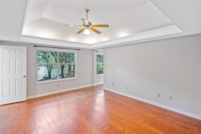 spare room featuring light wood-type flooring, a tray ceiling, baseboards, and a ceiling fan