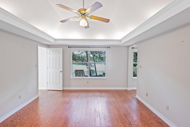 spare room with a tray ceiling, baseboards, light wood-style flooring, and crown molding