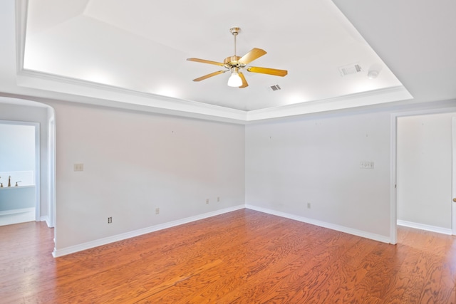 empty room featuring visible vents, baseboards, ceiling fan, light wood-type flooring, and a raised ceiling