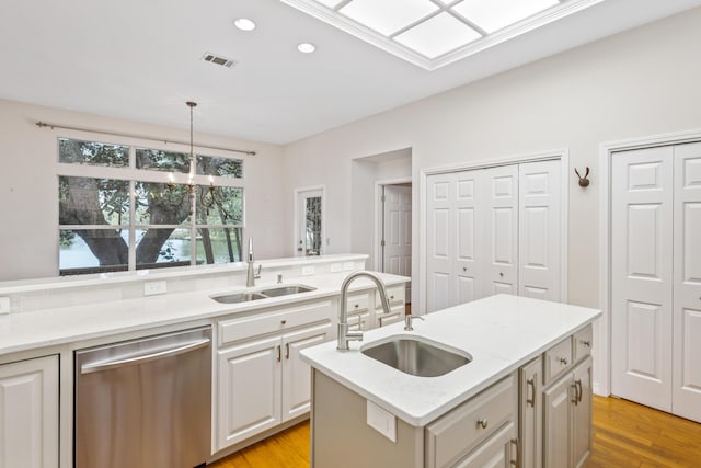 kitchen featuring stainless steel dishwasher, light countertops, hanging light fixtures, and a sink