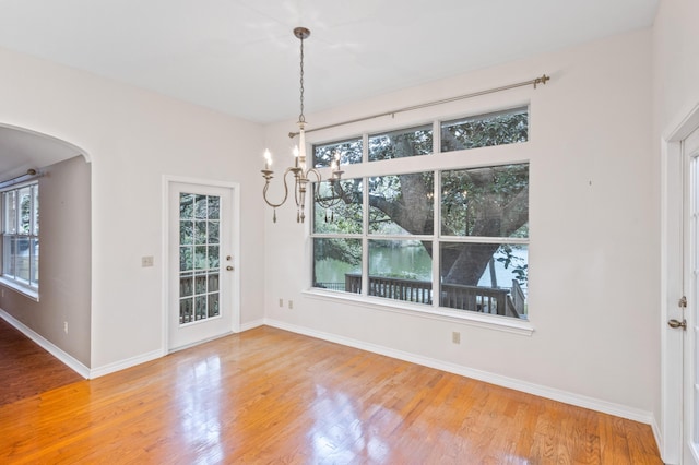 unfurnished dining area featuring baseboards, arched walkways, and wood finished floors