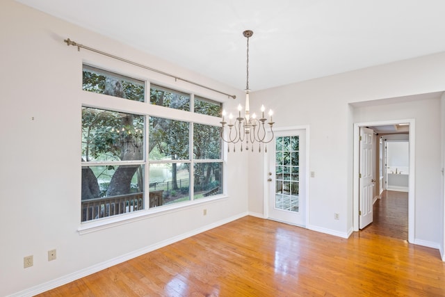 unfurnished dining area with a notable chandelier, baseboards, and light wood finished floors