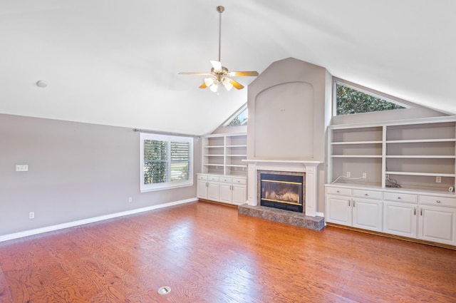 unfurnished living room featuring lofted ceiling, light wood-style flooring, a glass covered fireplace, baseboards, and ceiling fan