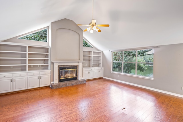 unfurnished living room with a glass covered fireplace, built in shelves, wood finished floors, and baseboards