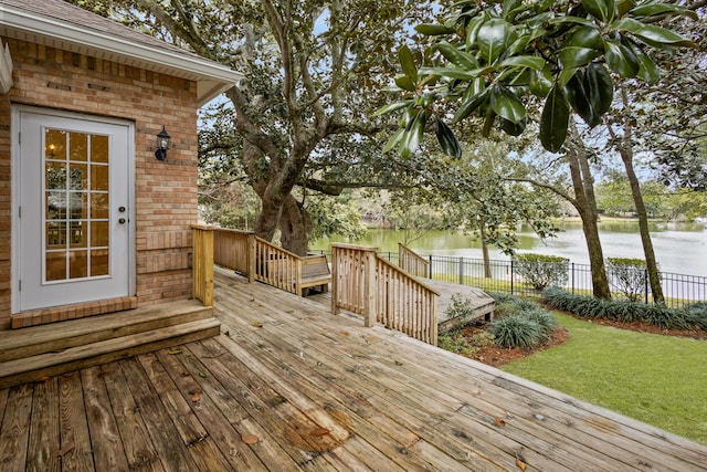 wooden terrace featuring fence, a water view, and a lawn