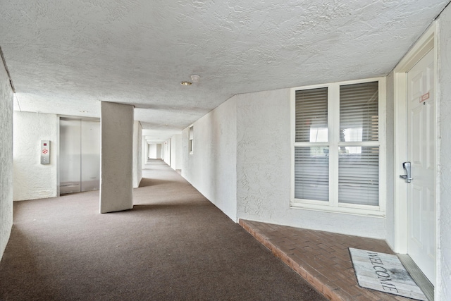 hall with a textured ceiling, a textured wall, carpet, and elevator