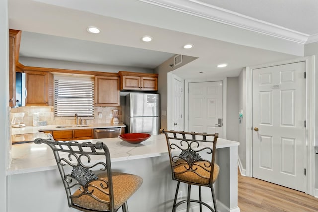 kitchen featuring stainless steel appliances, light wood-style floors, brown cabinetry, a sink, and a kitchen bar