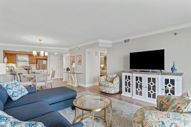 living room with crown molding, visible vents, an inviting chandelier, light wood-style floors, and baseboards