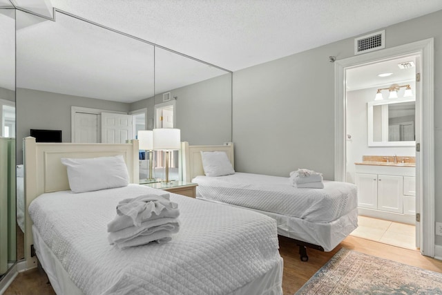 bedroom featuring ensuite bathroom, a textured ceiling, wood finished floors, a sink, and visible vents