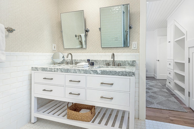 bathroom with double vanity, wallpapered walls, a sink, and a wainscoted wall