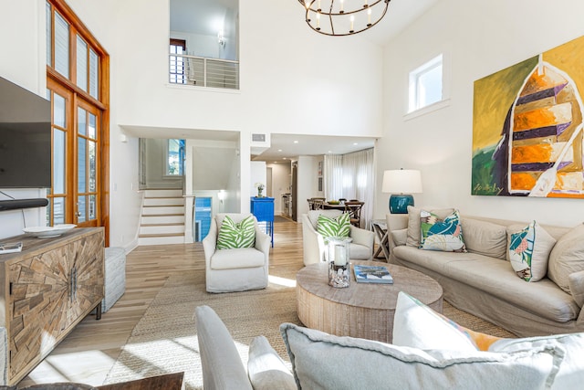 living area featuring a notable chandelier, a high ceiling, wood finished floors, visible vents, and stairs