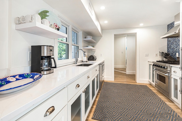 kitchen with open shelves, tasteful backsplash, stainless steel stove, a sink, and wall chimney range hood