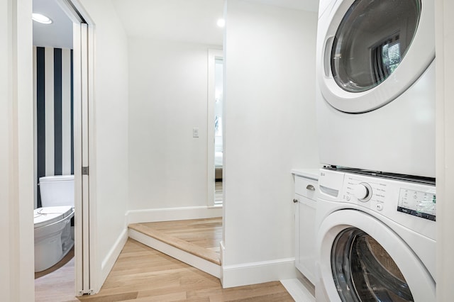 laundry room featuring stacked washer and dryer, light wood-type flooring, cabinet space, and baseboards