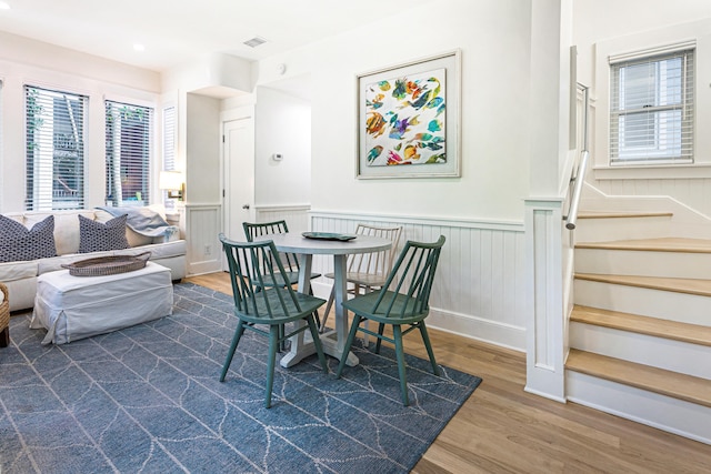 dining area with dark wood-style floors, visible vents, stairway, and wainscoting