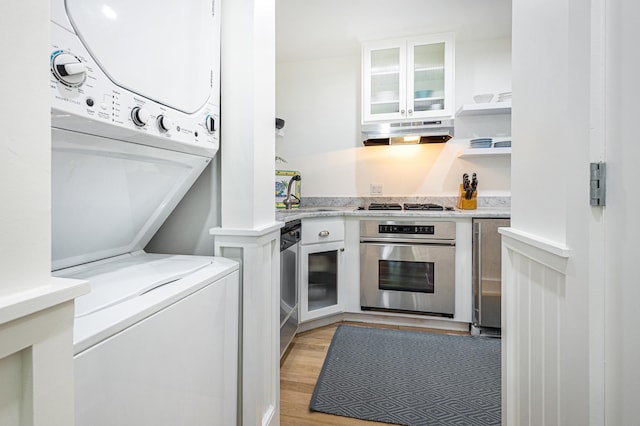 interior space featuring under cabinet range hood, appliances with stainless steel finishes, white cabinets, and stacked washer / drying machine