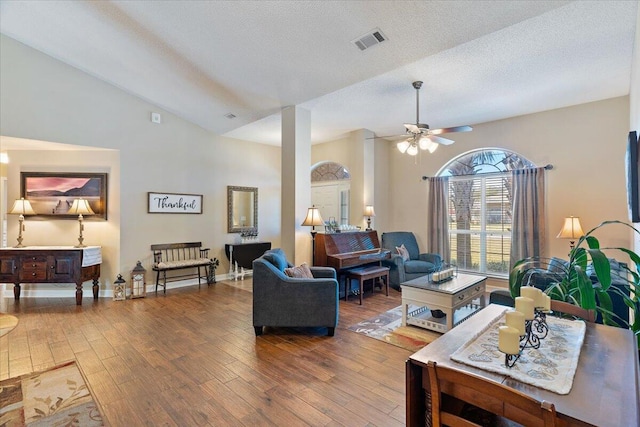 living area featuring visible vents, vaulted ceiling, a textured ceiling, wood finished floors, and baseboards