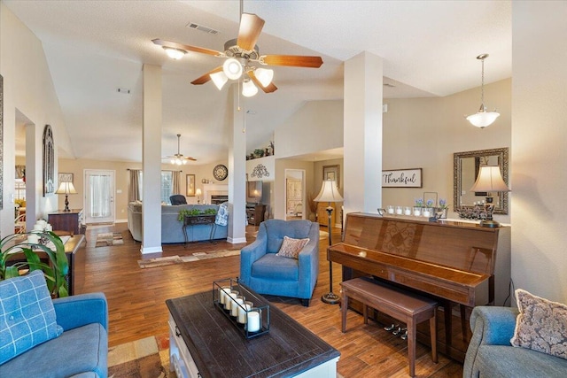 living room featuring high vaulted ceiling, a fireplace, visible vents, and wood finished floors