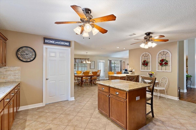 kitchen with light stone counters, a breakfast bar, a kitchen island, visible vents, and brown cabinetry