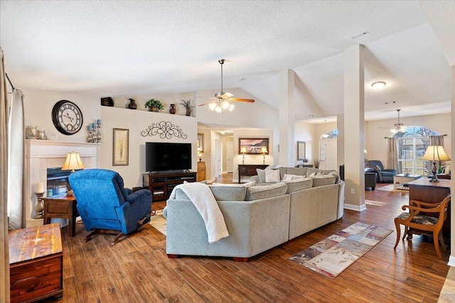 living area featuring lofted ceiling, a textured ceiling, a tiled fireplace, and wood finished floors