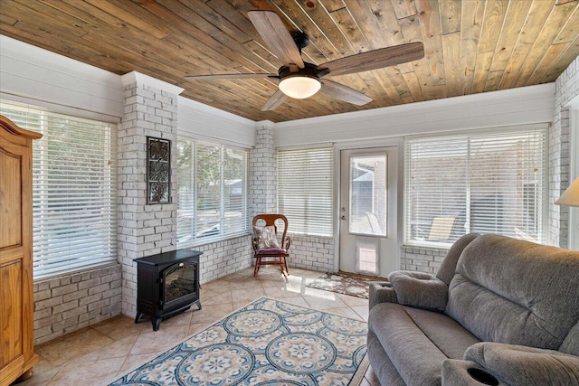 living area with light tile patterned floors, ceiling fan, brick wall, wood ceiling, and a wood stove