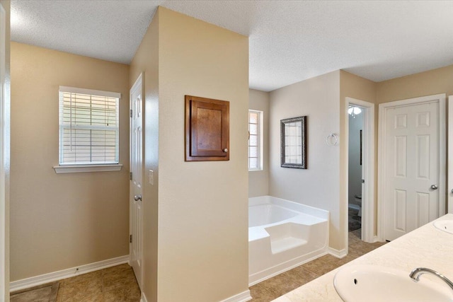 bathroom with a garden tub, double vanity, a sink, a textured ceiling, and baseboards