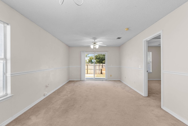 empty room featuring visible vents, light colored carpet, a textured ceiling, and baseboards