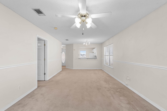 unfurnished room featuring light colored carpet, visible vents, baseboards, and ceiling fan with notable chandelier