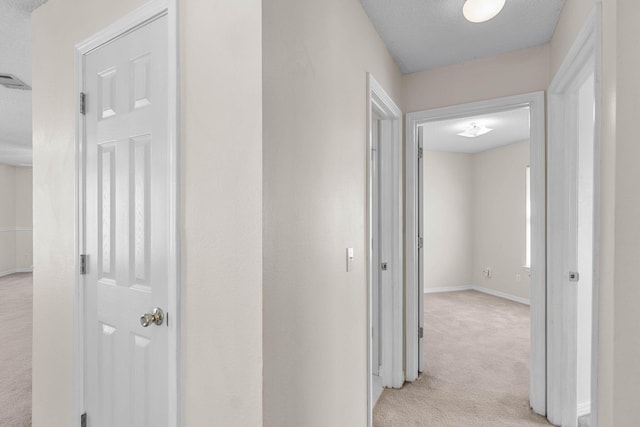 hallway with light carpet, baseboards, and a textured ceiling