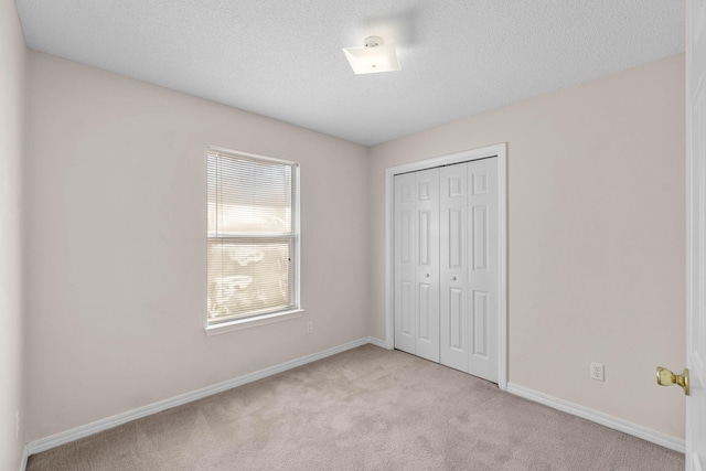 unfurnished bedroom featuring light carpet, a textured ceiling, baseboards, and a closet