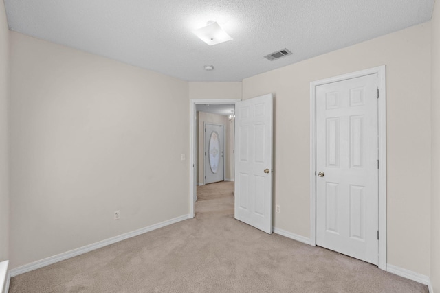 unfurnished bedroom featuring light carpet, a textured ceiling, visible vents, and baseboards