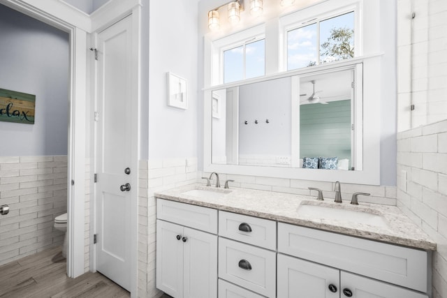 bathroom with a wainscoted wall, toilet, a sink, and tile walls