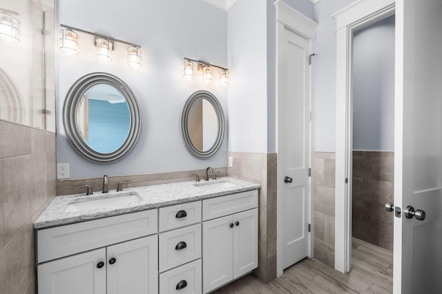 bathroom with double vanity, tile walls, a sink, and wood finished floors