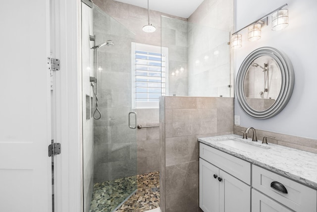 full bathroom with a stall shower, vanity, and tile walls